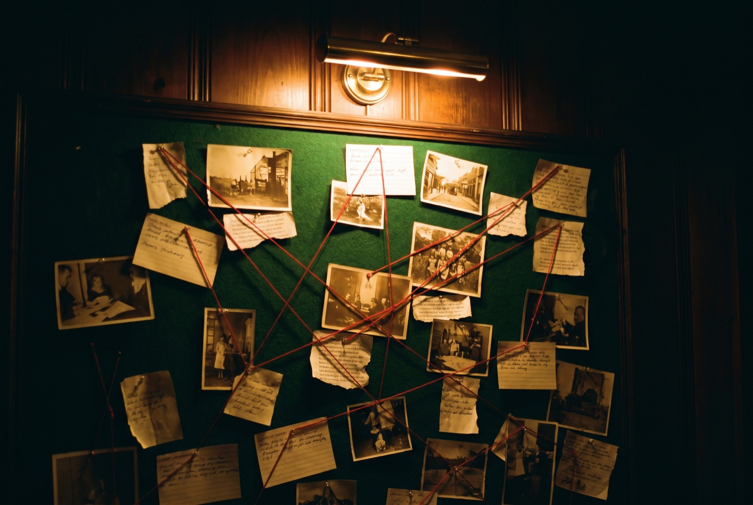 A detective's evidence board lit by a single brass picture light